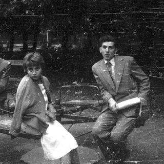 Three formally dressed people sit on a park bench.
