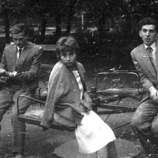 Three formally dressed people sit on a park bench.