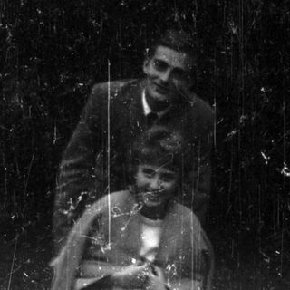 Here's a brief summary of the image: Woman seated, man standing nearby in a vintage scene.