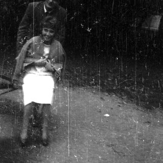 Here's a brief summary of the image: Woman seated, man standing nearby in a vintage scene.