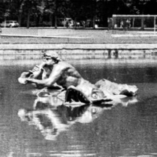 Statues of horses and riders reflected in a pond.