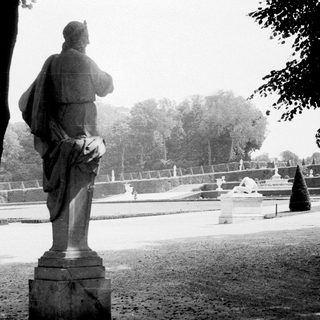 Statue in formal garden with distant landscaping and trees.