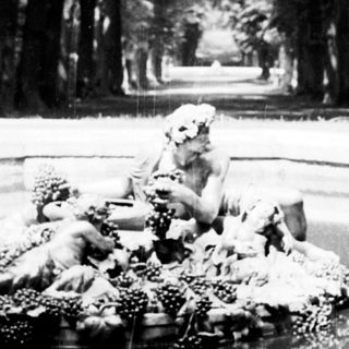 Statue in a fountain reflects in a long, tree-lined avenue.
