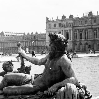 Statue of a man with a cherub, Versailles palace in background.