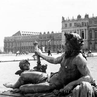 Statue of a man with a cherub, Versailles palace in background.