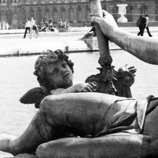 Statue of a man with a cherub, Versailles palace in background.