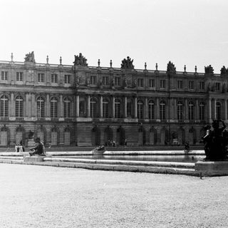 Grand palace facade with fountains and statues in a garden.