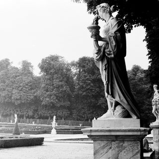Statue in formal garden with fountains and manicured hedges.