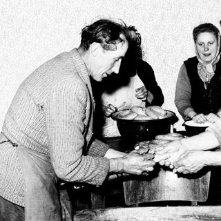 Family making bread in a humble, older kitchen setting.