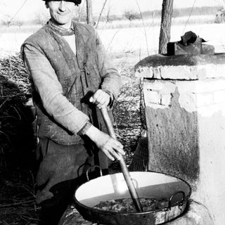 Man stirs contents in a large pan outdoors.