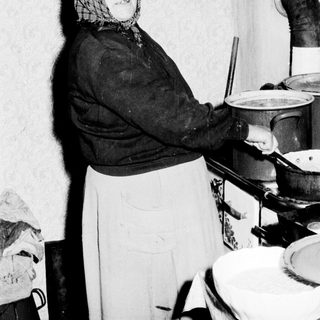 Woman in kitchen cooking, possibly in a rural setting.