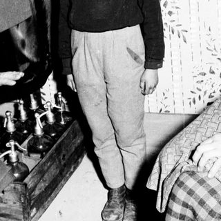 Young boy stands near medical equipment, possibly during wartime.