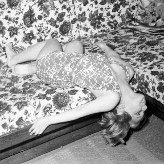 Here's a brief summary of the image: Woman lies on a floral-patterned couch, head tilted.