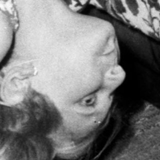 Here's a brief summary of the image: Woman lies on a floral-patterned couch, head tilted.