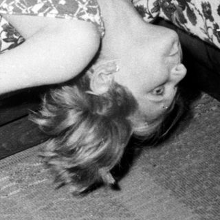 Here's a brief summary of the image: Woman lies on a floral-patterned couch, head tilted.