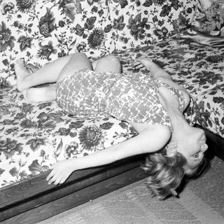 Here's a brief summary of the image: Woman lies on a floral-patterned couch, head tilted.