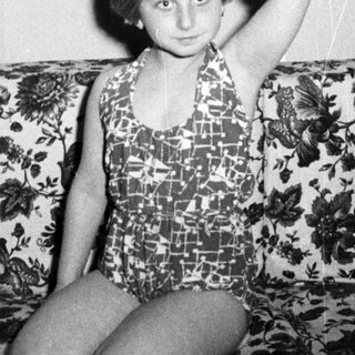 Girl in a swimsuit sits on a floral couch.