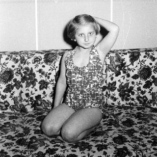 Girl in a swimsuit sits on a floral couch.