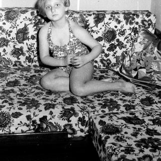 Girl in swimsuit sits on a patterned couch.