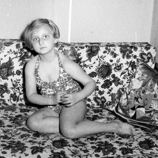 Girl in swimsuit sits on a patterned couch.
