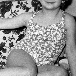 Young girl in a swimsuit sits on a floral sofa.