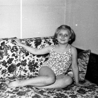 Young girl in a swimsuit sits on a floral sofa.