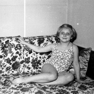 Young girl in a swimsuit sits on a floral sofa.