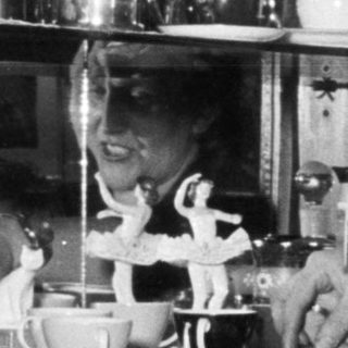 Child reaching for items in a cabinet, woman watching.