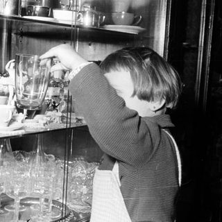 Boy reaches for a glass in a china cabinet.