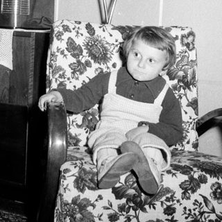 Here's a brief summary of the image: Young boy sits in a patterned chair, looking downwards.