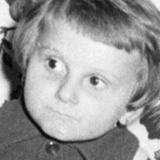 Here's a brief summary of the image: Young boy sits in a patterned chair, looking downwards.
