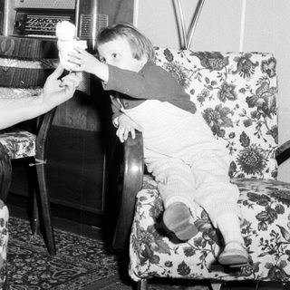 Baby reaching for something while seated in a chair.