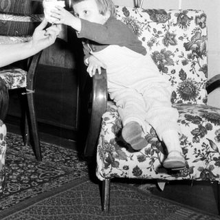 Baby reaching for something while seated in a chair.