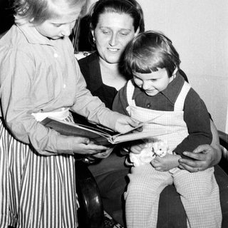 Woman reads to two children in a vintage setting.