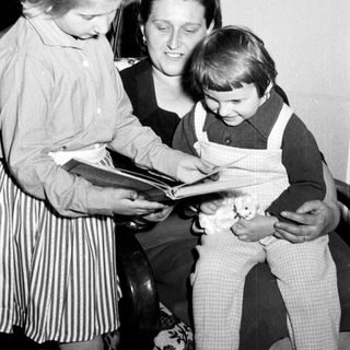 Woman reads to two children in a vintage setting.
