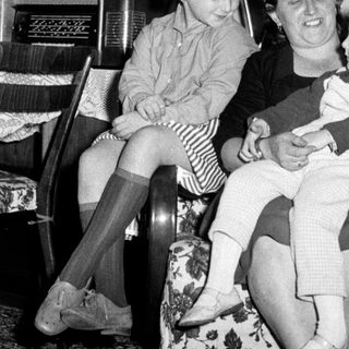 Woman seated with two children in a vintage living room.