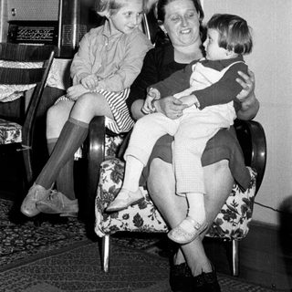 Woman seated with two children in a vintage living room.