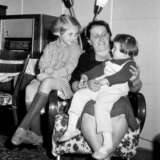 Woman seated with two children in a vintage living room.