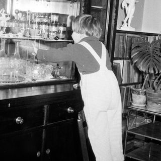 Child in overalls reaches for items on a shelf.