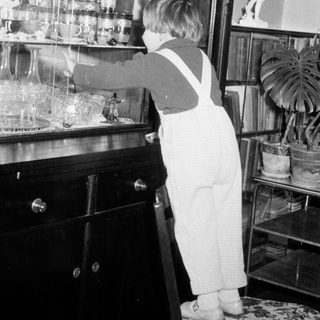 Child in overalls reaches for items on a shelf.