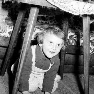 Black and white photo of a child playing under a table.