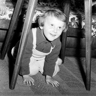 Black and white photo of a child playing under a table.