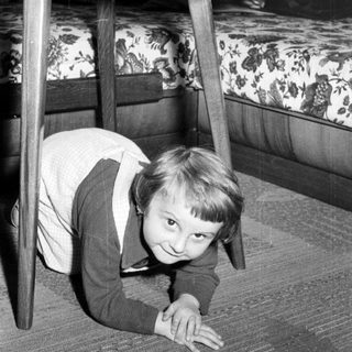 Black and white photo of a child crawling under a table.