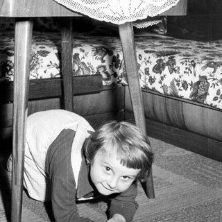 Black and white photo of a child crawling under a table.