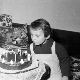 Here's a brief summary of the image: Child stares at a cake with lit candles.