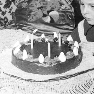 Here's a brief summary of the image: Child stares at a cake with lit candles.
