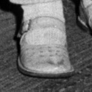 Here's a brief summary of the image: Child stands near a cake, wearing overalls.