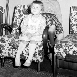 Two children seated on chairs in a vintage room.