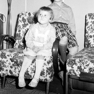 Two children seated on chairs in a vintage room.