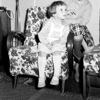 Here's a brief summary of the image: Two young girls seated in floral armchairs.